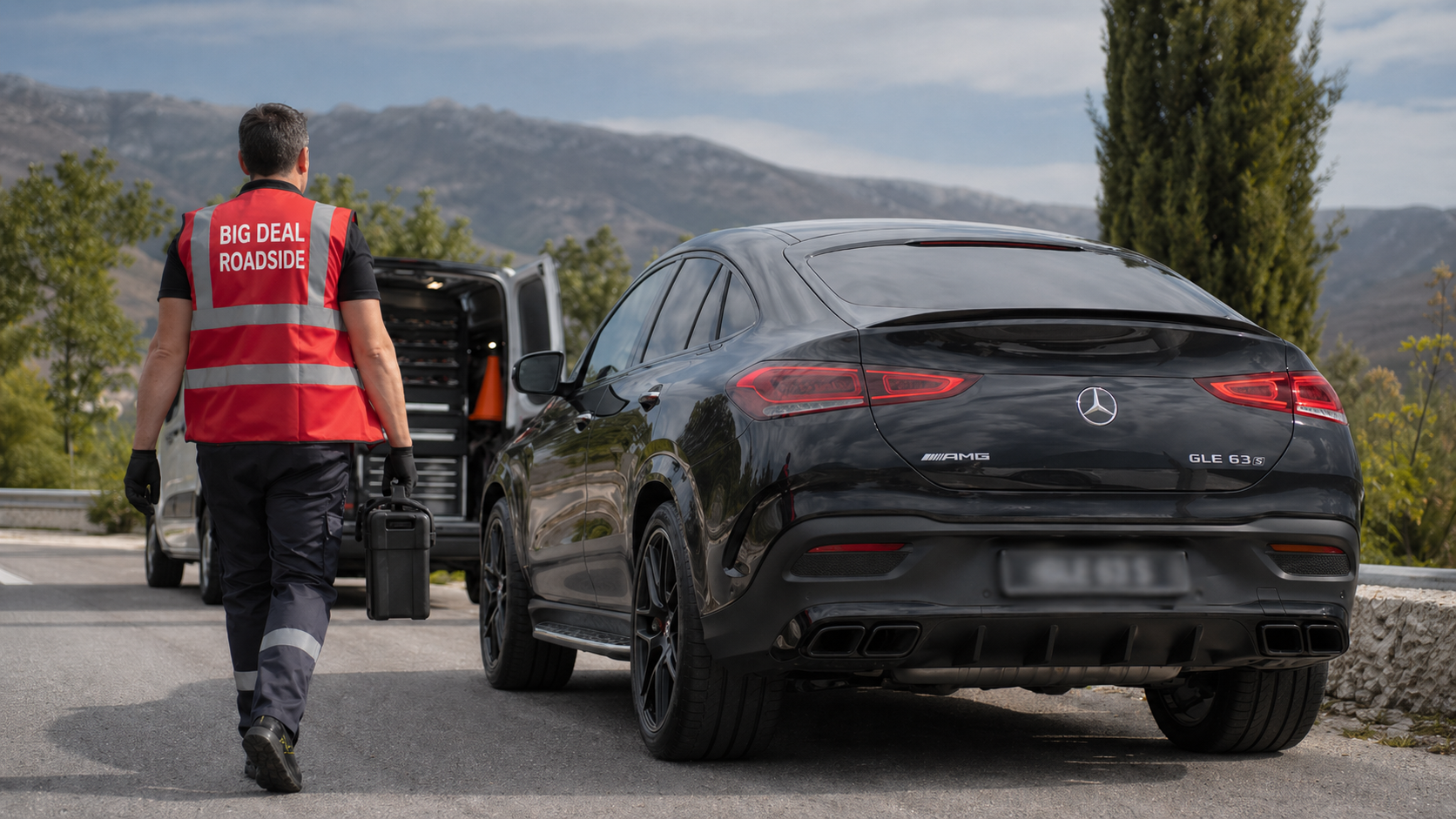 A Big Deal Roadside technician in a red high-visibility vest carrying a tool case toward a black Mercedes-Benz AMG GLE 63 S parked beside a service van on a mountain road